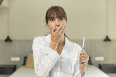 Genç ve güzel bir kadın ağzını eliyle kapatıyor ve şok olmuş ya da şaşırmış bir ifade takınıyor. gargara konsepti