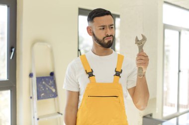 Arap yakışıklı Arap adam gülümsüyor ve kendine güveni tam bir ifadeyle bakıyor. İngiliz anahtarı olan bir tamirci.