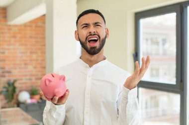 Elleri havada bağıran genç bir adam. domuz kumbarası konsepti