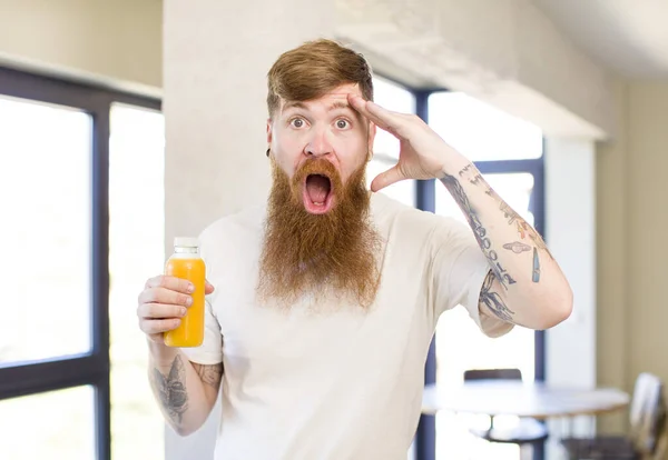 红头发的男人看上去很快乐 对橙汁瓶感到惊讶和惊讶 — 图库照片