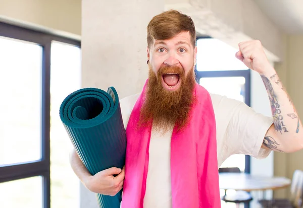 红头发的男人感到震惊 笑着用瑜伽垫庆祝成功 健身概念 — 图库照片