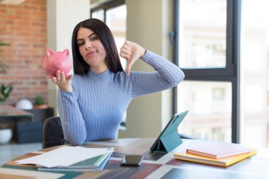 Güzel, genç bir kadın kendini kötü hissediyor, baş parmağını kaldırıyor. Domuz kumbarası konsepti
