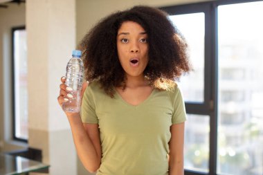 Oldukça afro siyahi bir kadın son derece şok olmuş ve şaşırmış hissediyor. su şişesi kavramı