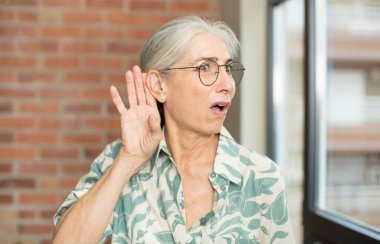 Kıdemli güzel kadın ciddi ve meraklı görünüyor, dinliyor, gizli bir konuşma veya dedikodu duymaya çalışıyor, kulak misafiri oluyor.