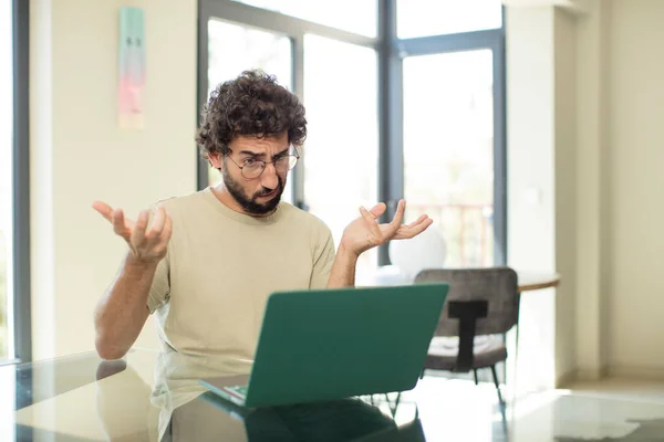 一个留着胡子的年轻人 带着笔记本电脑 看上去困惑 困惑和紧张 在不同的选择之间徘徊 感到不确定 — 图库照片