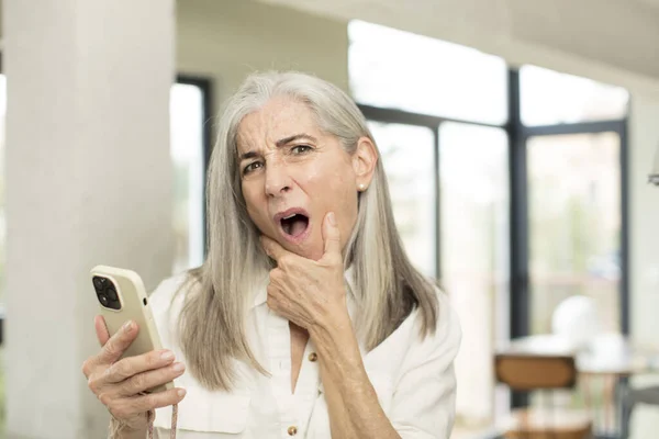 Pretty Senior Woman Mouth Eyes Wide Open Hand Chin Smartphone — Stock Photo, Image
