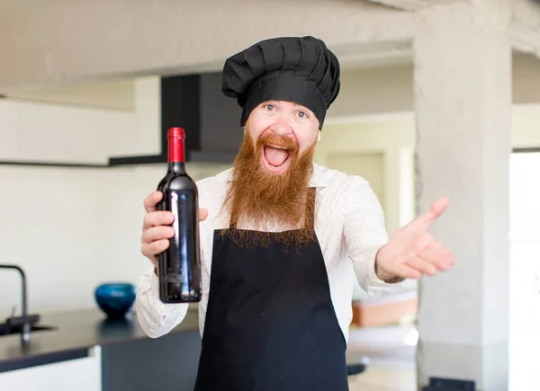 赤い髪の男は喜んで笑顔でワインボトルでコンセプトを提供または示す シェフのコンセプト — ストック写真
