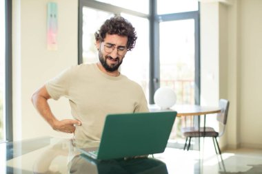 Dizüstü bilgisayarı olan sakallı genç bir adam endişeli, hasta, hasta ve mutsuz hissediyor.