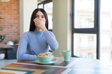 Güzel genç bir kadın ağzını eliyle kapatıyor ve şok olmuş ya da şaşırmış bir ifade takınıyor. kahvaltı kavramı