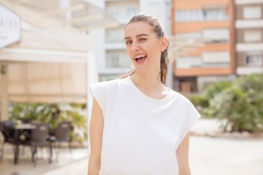 Güzel bir kadın mutlu ve arkadaş canlısı görünüyor, gülümsüyor ve sana olumlu bir tavırla göz kırpıyor.