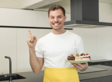 Neşeli bir şekilde gülümsüyor, mutlu hissediyor ve bir tarafı işaret ediyor. Ev yapımı kek konsepti