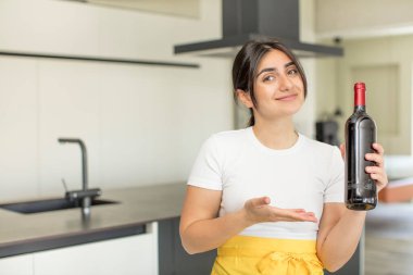 Genç bir kadın neşeyle gülümsüyor, mutlu hissediyor ve bir konsept gösteriyor. şarap şişesi konsepti