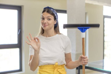 young pretty woman feeling happy, showing approval with okay gesture. windows washer concept