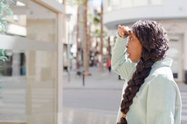 afro güzel siyah kadın şaşkın ve şaşkın bakıyor, el üstünde uzak bakıyor, izliyor ya da arıyor
