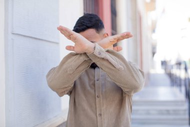 Genç ve yakışıklı bir adam elleriyle yüzünü kapatıyor ve kamerayı durdurmak için diğer elini öne koyuyor. Fotoğraf ya da resimleri reddediyor.