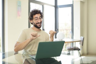 Genç, sakallı, dizüstü bilgisayarlı, neşeli gülümseyen, yandan fotokopi makinesini gösteren mutlu ve tatmin olmuş bir adam.