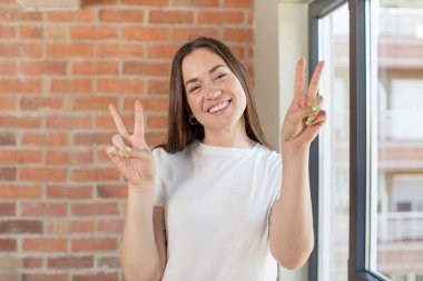 young adult pretty woman smiling and looking happy, friendly and satisfied, gesturing victory or peace with both hands