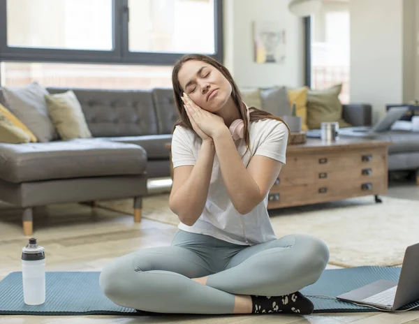 Genç yetişkin kadın sabahın erken saatlerinde tembel tembel yoga yapıyor, uykulu, yorgun ve sıkkın görünüyor.