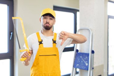 Genç ve yakışıklı bir adam kendini kötü hissediyor, baş parmağını kaldırıyor. Testereli tamirci.