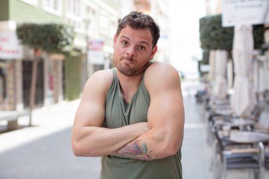 Yakışıklı adam omuz silkiyor, şaşkın ve kararsız hissediyor, kolları bağlı ve şaşkın bir şekilde şüpheye düşüyor.