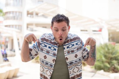 Yakışıklı ve ağzı açık bir adam iki eliyle aşağıya bakıyor. Şok olmuş, şaşırmış ve şaşırmış görünüyor.