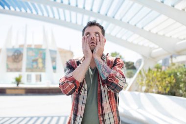 Yakışıklı adam şok olmuş ve korkmuş hissediyor. Elleri yanaklarında sıkılmış görünüyor.