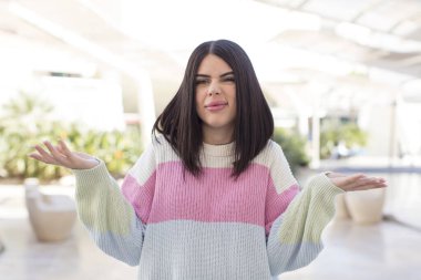 Şaşkın, kafası karışmış ve stresli görünen genç bir kadın. Farklı seçenekler arasında merak ediyor, kararsız.