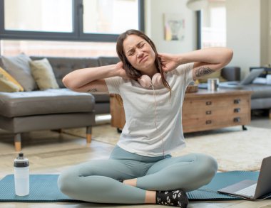 Yoga yapan genç bir kadın endişeli, hasta, hasta ve mutsuz, ağrılı bir boyun ağrısı çekiyor.