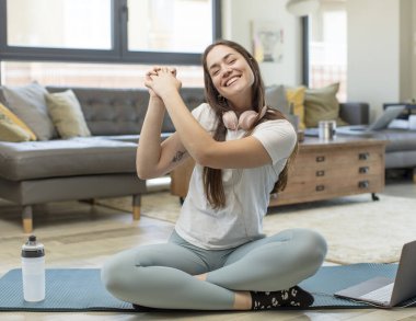 Genç yetişkin kadın yoga yapıyor. Mutlu, şaşırmış ve gururlu. Büyük bir gülümsemeyle başarıyı bağırıyor ve kutluyor.