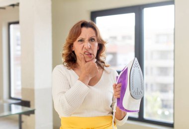 Orta yaşlı, ağzı açık ve elleri çenesinde olan güzel bir kadın. Temizlikçi ve çamaşır konsepti