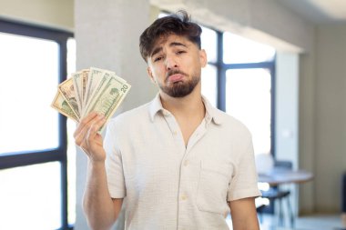 Genç ve yakışıklı bir adam üzgün ve mızmızlanıyor. Mutsuz bir bakışı var ve ağlıyor. Dolar banknotları konsepti