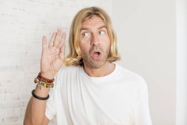 Genç sarışın yetişkin bir adam ciddi ve meraklı görünüyor, dinliyor, gizli bir konuşma veya dedikodu duymaya çalışıyor, kulak misafiri oluyor.