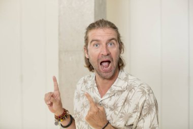 Genç sarışın yetişkin bir adam neşeli ve şaşırmış hissediyor, şok olmuş bir ifadeyle gülümsüyor ve bir tarafı işaret ediyor.