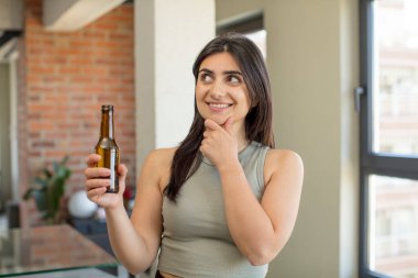 Gülümseyen mutlu, kendine güvenen, elleri çenesinde genç bir kadın. bira şişesi