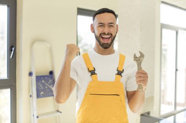 Arap yakışıklı Arap adam şok olmuş hissediyor, gülüyor ve başarıyı kutluyor. İngiliz anahtarı olan bir tamirci.