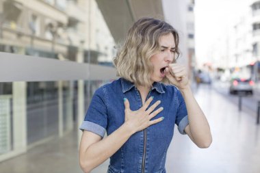 Gırtlağı ağrıyan, grip semptomları gösteren, ağzı kapalı öksüren güzel bir kadın.
