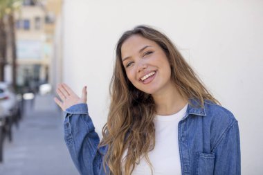 Güzel İspanyol kadın mutlu ve neşeyle gülümsüyor, el sallıyor, seni selamlıyor ya da veda ediyor.