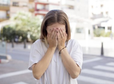 Güzel genç bir kadın üzgün, hayal kırıklığına uğramış, gergin ve depresif hissediyor. İki eliyle yüzünü kapatıyor, ağlıyor.