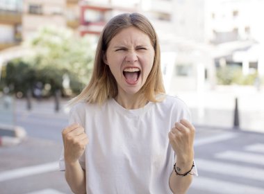 Güzel genç bir kadın sinirli, sinirli, kızgın bakışlar ve sıkı yumruklar ile agresif bir şekilde bağırıyor.