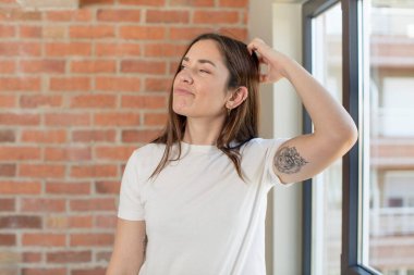 Genç, güzel bir kadın kafası karışmış ve kafası karışmış, başını kaşıyor ve yan tarafa bakıyor.