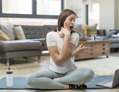 Yoga yapan genç bir kadın şok edici bir ifadeyle şaşırmış ve yan tarafı işaret ediyor.