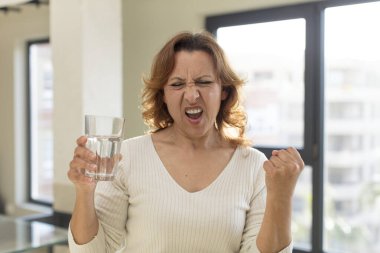 Orta yaşlı, güzel bir kadın sinirli, sinirli ve sinirli görünüyor. su bardağı