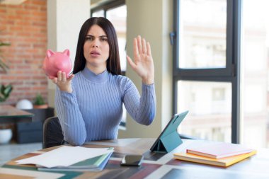 Güzel, genç bir bayan ciddi görünüyor. Avuç içini gösteriyor. Durdurma hareketi yapıyor. Domuz kumbarası konsepti