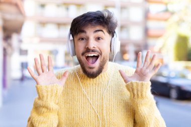 Genç yakışıklı adam kendini mutlu hissediyor ve inanılmaz bir şeye hayret ediyor. kulaklıkla müzik dinlemek