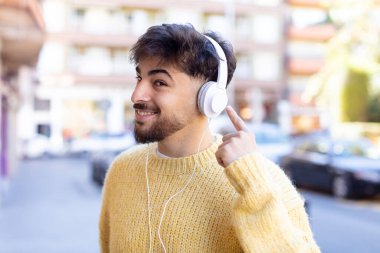 Genç yakışıklı adam neşeyle gülümsüyor, mutlu hissediyor ve bir konsept gösteriyor. kulaklıkla müzik dinlemek