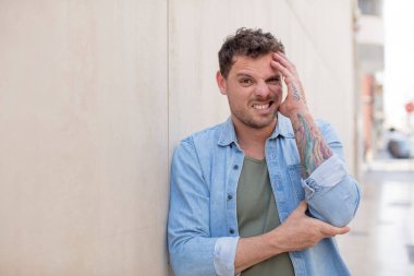 Yakışıklı adam şok ve inançsızlık içinde, elleri yanağında ve kolları çaprazlanmış, sersemlemiş ve şaşırmış hissediyor.