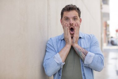 Yakışıklı adam şok olmuş ve korkmuş hissediyor, ağzı açık ve elleri yanaklarında korkmuş görünüyor.