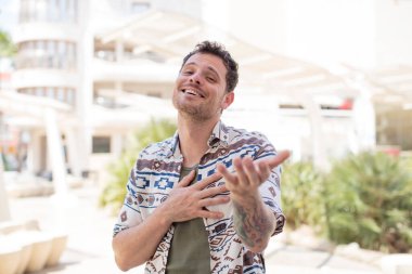 Yakışıklı adam kendini mutlu ve aşık hissediyor, bir eli kalbinin yanında gülümsüyor ve diğer eli önde uzanıyor.