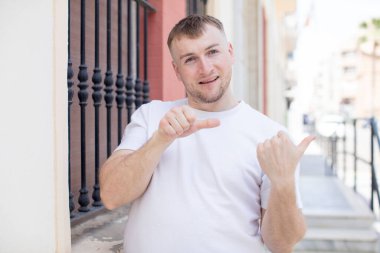 Yakışıklı adam neşeyle gülümsüyor ve tesadüfen fotokopi alanını işaret ediyor, mutlu ve tatmin olmuş hissediyor.