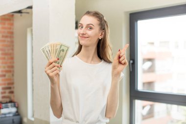 Neşeli bir şekilde gülümsüyor, mutlu hissediyor ve bir tarafı işaret ediyor. Dolar banknotları konsepti